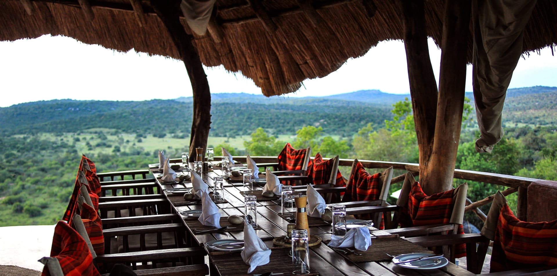 Long dinner table under a thatched roof overlooking the Ugandan hills