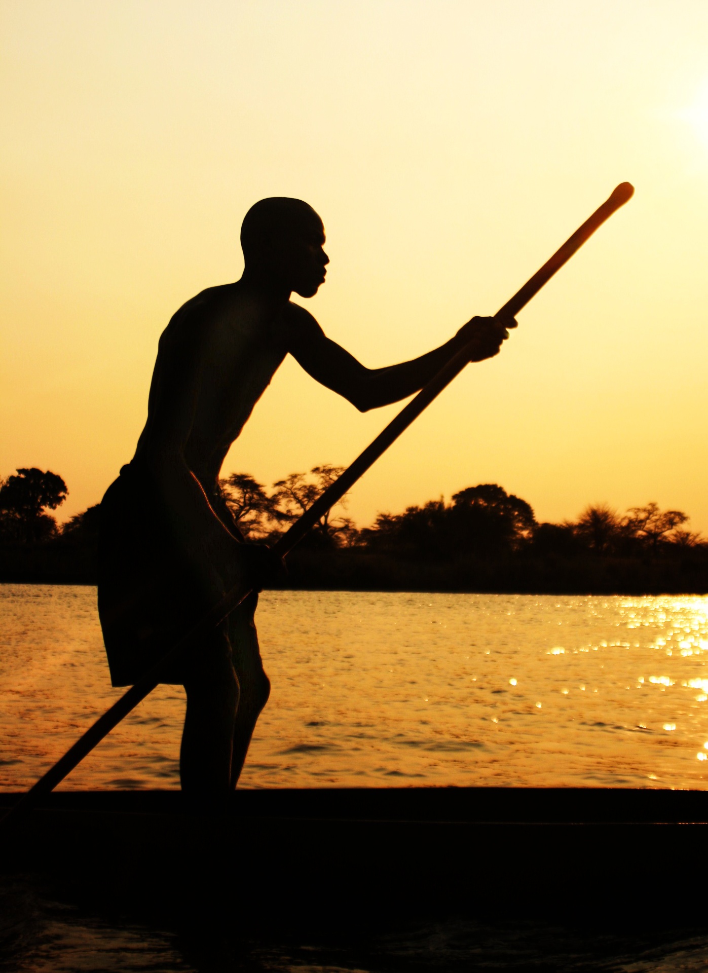 Mokoro poler silhouetted against an Okavango sunset